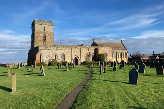 Bamburgh St Aidan Church photographed from across a grassy churchyard