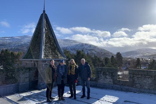 A photograph of four people on top of a church with blue skies and mountains behind