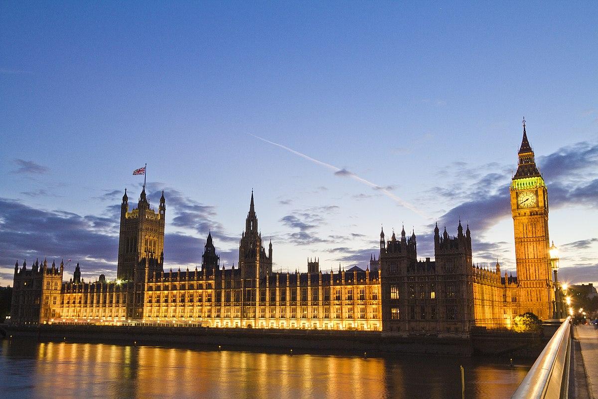 The UK Houses of Parliament lit up with a blue sky behind and part of the river Thames visible 