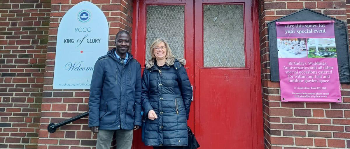 A photograph of two people standing outside the front door of a church