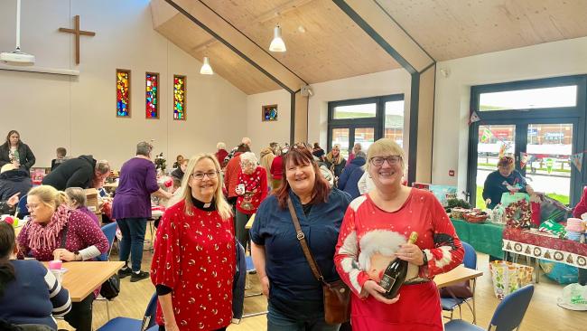 A group of three women stand inside Redcar St Hilda Church with tables of other people behind