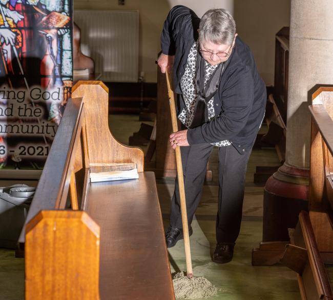 A woman mopping the floor of a church between two pews