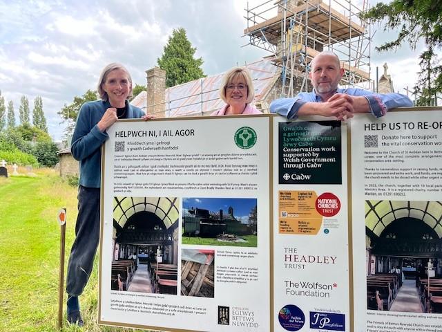 Three people standing behind a large sign