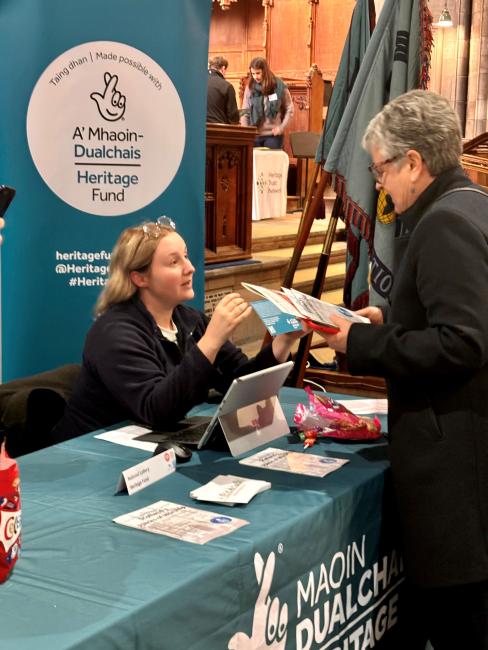 A woman picks up a leaflet at a stall where another woman is sat down