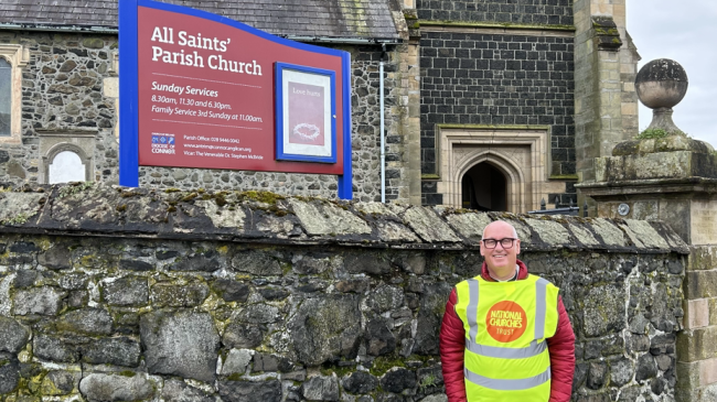 A man in a high-vis jacket stands outside a church in front of a wall