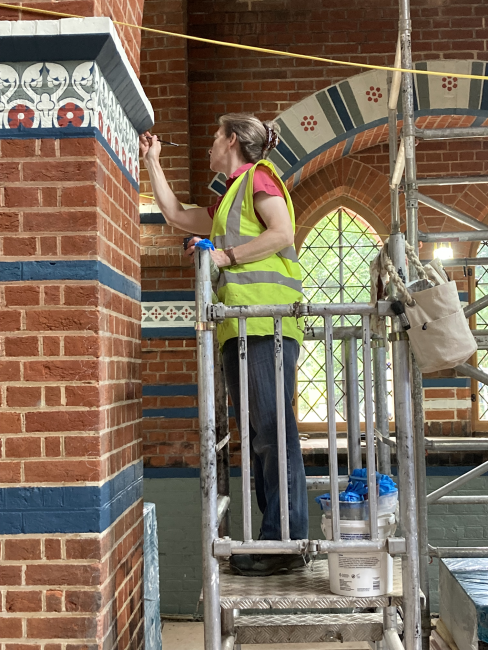 A woman in a high-vis jacket paints details inside a church